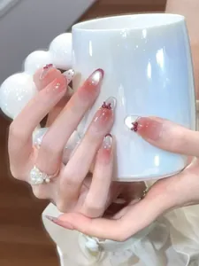 Detail of long oval pink gradient press-on nails with red bows and pearl ring accents