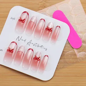 Close-up of pink gradient press-on nails with red bows and French tips in a set