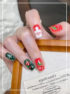 Gros plan de faux ongles de Noël courts avec motifs Père Noël, flocons et feuilles de houx