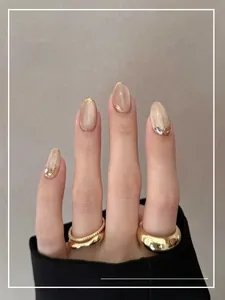 Detail of short oval press-on nails in nude tones with gold foil and glitter accents