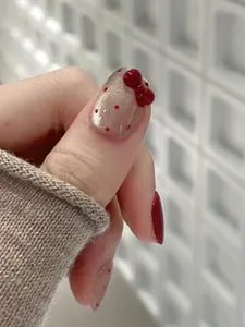 Detail of burgundy press-on nails with 3D red bow, cat-eye shimmer, and polka dot patterns