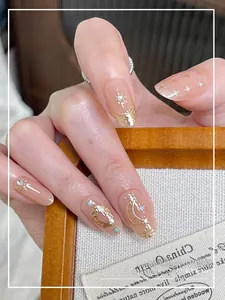 Close-up of pink press-on nails with gold sun and moon metal charms and tiny rhinestones