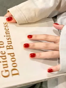 Glossy cherry red press-on nails in short round shape shown in a lifestyle scene