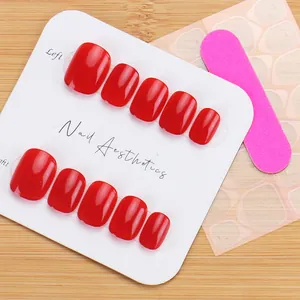 Short cherry red press-on nails set with adhesive tabs and nail file on a wood background