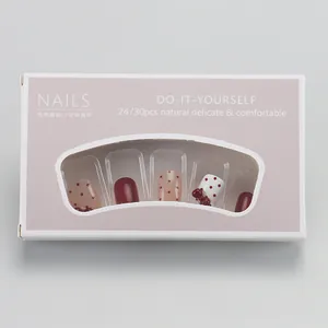 Detail view of burgundy press-on nails with red bows and dots in a window gift box