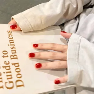 Glossy cherry red short round press-on nails shown on hands holding a vintage book