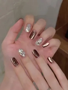 Detail of short bronze and silver glitter press-on nails with luxury rhinestone accents