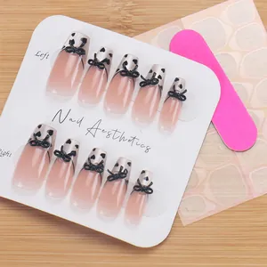 Detail of pink gradient press-on nails with 3D black bows and hearts on wooden background