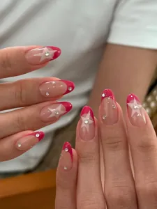 Dettaglio di unghie a mandorla con punte French magenta, stelle bianche e strass lucidi