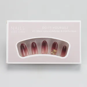 Détail de faux ongles dégradés marron-rouge avec strass dans une boîte cadeau rose