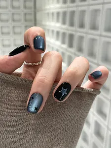 Detail van korte cat-eye kunstnagels met zwart-grijs verloop en zilveren sterpatronen