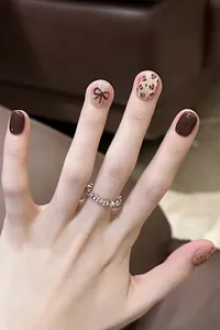 Detalle de uñas de leopardo y marrón oscuro con lazo dorado en 3D y un anillo de plata