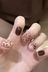 Primer plano de uñas postizas cortas marrones con estampado de leopardo y lazo