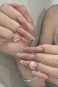Close-up of almond-shaped press-on nails with pink ombre and 3D rhinestone heart accents
