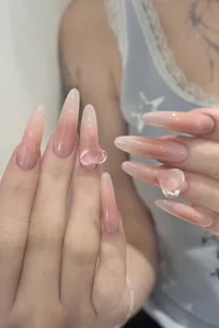 Macro detail of long almond-shaped ombre pink press-on nails with 3D crystal hearts