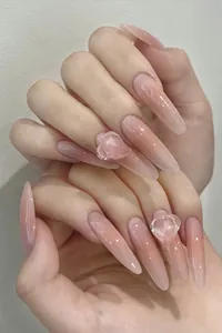 Detail view of long almond press-on nails with nude pink gradient and 3D heart charms