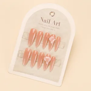 Detail of nude pink press-on nails with 3D crystal hearts on a product display card