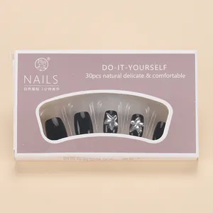 Detail of glossy black short press-on nails with silver floral accents in purple box