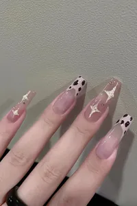 Detail of long ballerina nails featuring cow print tips and gold glitter star designs