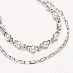 Macro detail of silver paperclip chain with pearl insets on a textured grey surface