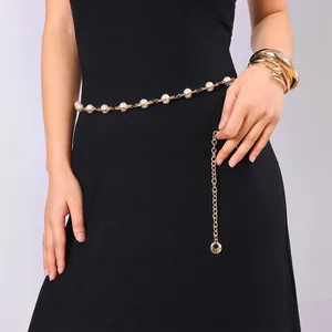 Elegant gold metal waist chain with white pearls on a black dress, front view