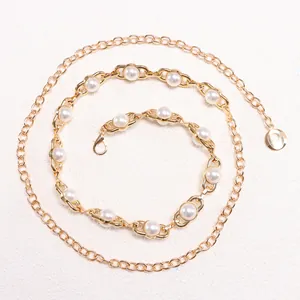 Detailed close-up of golden metal chain belt with elegant white pearls and lobster clasp