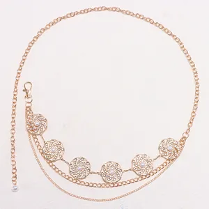 Detail einer mehrlagigen goldenen Bauchkette mit hohlen Blumenanhängern und weißen Perlen