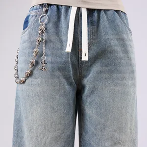 Detail of silver skull and fleur-de-lis metal chain on light blue washed denim jeans