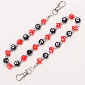 Dettaglio catena per pantaloni con dadi rossi, perle 8-ball nere e strass argentati
