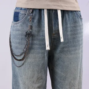 Detail of light blue jeans with multi-layer metal chains and a black spider pendant