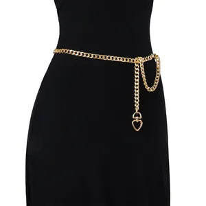 Detail of a thin gold metal waist chain featuring a heart-shaped pendant on a black dress