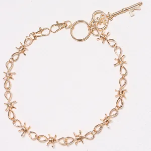 Detail van gouden prikkeldraad riemketting met kroonsleutel hanger en karabijnsluiting