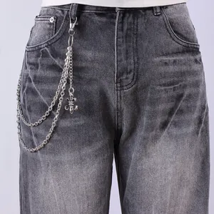 Detail of silver multi-layered metal chain with fleur-de-lis pendant on washed denim jeans