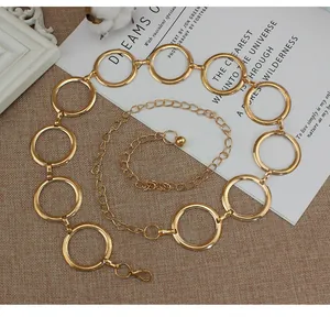 Detalle de una cadena de cuerpo dorada con anillos geométricos y cierre de mosquetón