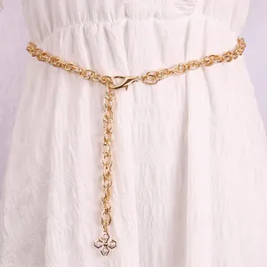 Gouden schakelketting riem met strass klavertje hanger gedragen op witte kledingstukken