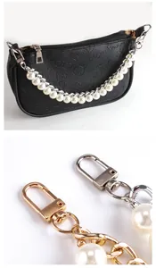 Detail einer geprägten schwarzen Tasche mit Perlenkette und Metallkarabinern