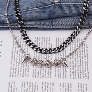 Close-up of layered silver cuban link chain with metallic spike and bead pendants on denim