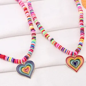 Detailaufnahme von Regenbogenperlen und goldenem Herzanhänger mit buntem Emaille