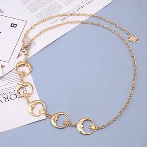 Détail d'une chaîne de taille dorée avec des pendentifs lune et un charm soleil en métal