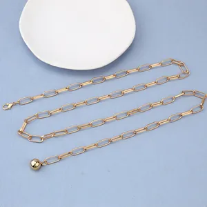 Chaîne de taille trombone dorée avec pendentif boule sur fond bleu texturé élégant