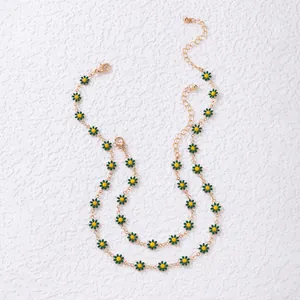Vue détaillée du collier double chaîne dorée avec pendentifs marguerites en émail vert