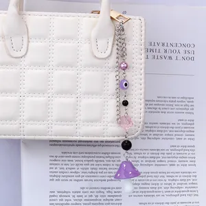 Detail of purple mushroom and evil eye charm pendant hanging on a white quilted bag