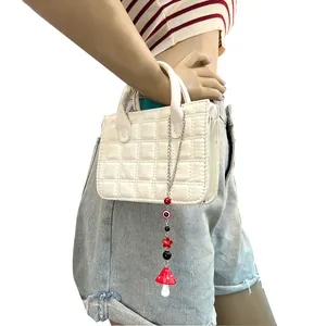 Detalle de mini bolso acolchado blanco con colgantes de hongo y ojo turco de colores