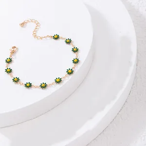 Minimalist gold daisy bracelet with green petals and yellow center on stone platforms