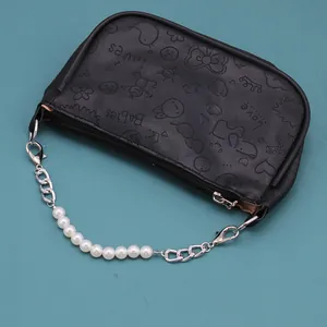 Detalle de un bolso negro de cuero sintético con patrones en relieve y asa de perlas