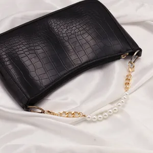 Detalle de cadena de perlas y metal dorado en bolso negro con diseño de cocodrilo