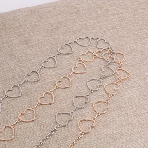 Dettaglio della catena a maglie a cuore cavo in finiture argento e oro su sfondo lino