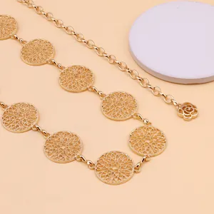 Detail of gold metal waist chain with filigree circles and a rose pendant on peach background