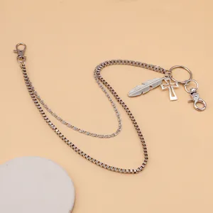 Detail of double-layer metal waist chain with cross and feather pendants on marble