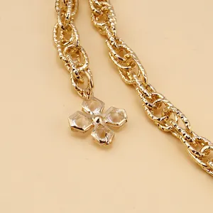 Detail of golden textured metal chain with a clear clover charm and gold-edged border